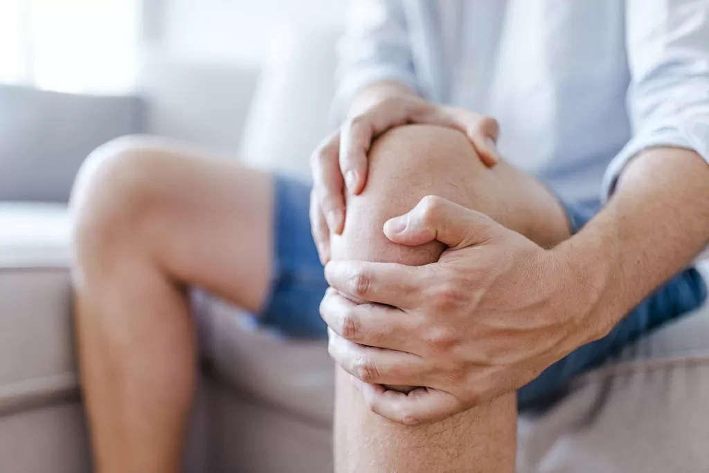 Man suffering from knee pain sitting sofa